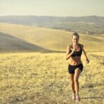 cheerful-sportswoman-running-along-hill-in-summer